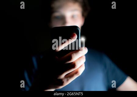 Ein junger attraktiver Mann nutzt in einem dunklen Raum spät in der Nacht das Handy Stockfoto