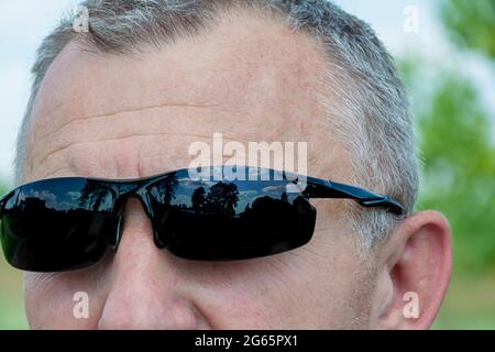 Männergesicht in dunkler Sonnenbrille, Nahaufnahme, verschwommener Hintergrund mit Bokeh-Elementen. Stock-Fotografie. Stockfoto