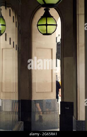 Blick auf den überdachten Gang neben dem modernen luxuriösen Arcade-Gebäude mit vertikalen Linien, teilweisem Blick auf eine Person und kunstvollem Lichtreflek Stockfoto