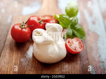 Burrata-Käse auf Holzbrett. Weicher Käse mit Tomaten und Basilikumblättern auf Holztisch. Leckere Burrata mit halber Tomate. Stockfoto