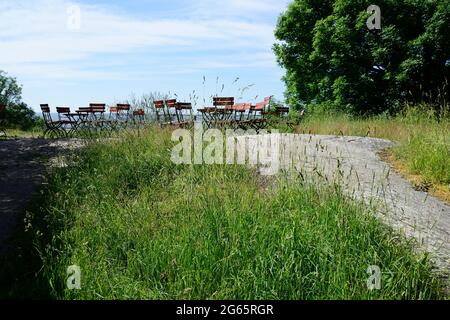 Stühle und Tische im Freien zwischen Gras und Bäumen mit Blick auf das Meer Stockfoto