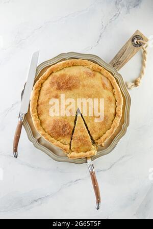 Fertige Schweizer Torte mit Mangold, Reis, Zwiebeln und Pinienkernen auf einem Holzständer auf weißem Marmor. Flach liegend Stockfoto