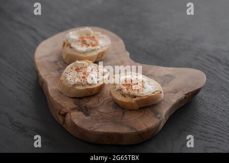 Baguette-Scheiben mit Frischkäse und Kräutern auf Olivenholzplatte, flacher Fokus Stockfoto