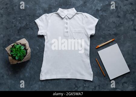 Weißes leeres Polo-T-Shirt und Notizbuch-Modell auf dunklem Hintergrund. Unbeschriftete Baumwolle mit unifarbenem Hemdkragen für kreatives Design. Kinderschule Lässige Kleidung Stockfoto