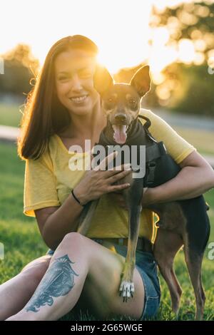 Schöne Frau sitzt und hält ihren Hund im Park Stockfoto