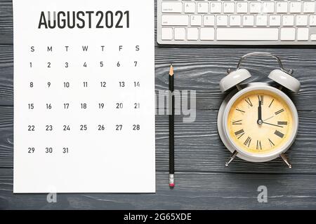 Papierkalender, Wecker, Tastatur und Bleistift auf dunklem Holzhintergrund Stockfoto