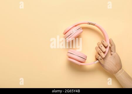 Holzhand mit modernen Kopfhörern auf farbigem Hintergrund Stockfoto