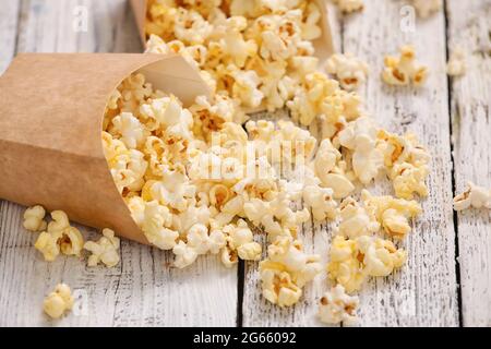 Papiertüten mit leckerem Popcorn auf hellem Holzhintergrund Stockfoto