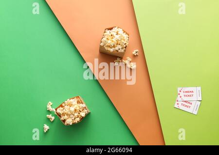 Papiertüten mit leckerem Popcorn und Kinokarten auf farbigem Hintergrund Stockfoto