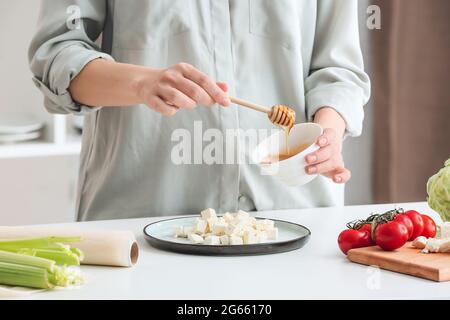 Frau gießt Honig auf den Feta-Käse auf den Teller, Nahaufnahme Stockfoto