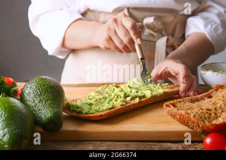 Frau bereitet leckeres Sandwich mit Avocado auf dem Tisch zu Stockfoto
