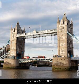 London, Greater London, England - 26 2021. Juni: Zwei rote Doppeldeckerbusse überqueren die Tower Bridge mit einem dramatischen Himmel darüber. Stockfoto