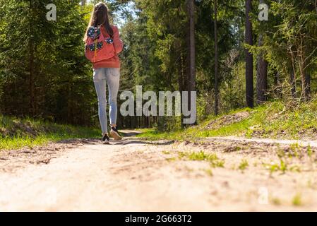 Ein junges Mädchen mit Rucksack zu Fuß entlang Weg durch den Wald während des Sommers. Hipster Lifestyle und Solo Trip.Rückansicht. Stockfoto