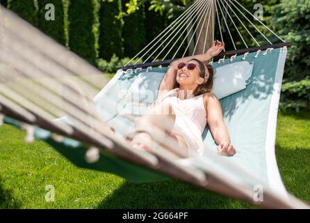Junge Frau, die in einer Hängematte liegt, die im Garten im Freien ruht. Attraktive Mädchen lächeln entspannend im Urlaub. Stockfoto