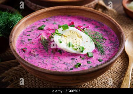 Kaltes Borscht, Sommerrübensuppe mit frischer Gurke, gekochtem Ei und gebackenen Kartoffeln auf Holztisch. Traditionelle europäische Küche, leckeres Mittagessen. Stockfoto