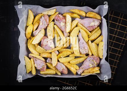 Rohe Hähnchenschenkel und Kartoffelkeile in Gewürzen auf einem zum Backen vorbereiteten Backblech. Draufsicht, flach liegend Stockfoto