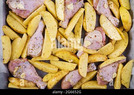 Rohe Hähnchenschenkel und Kartoffelkeile in Gewürzen auf einem zum Backen vorbereiteten Backblech. Draufsicht, Textur Stockfoto