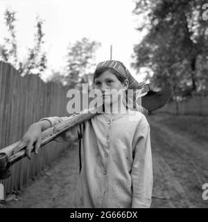 Sozialistische Republik Rumänien, ca. 1975. Junges Mädchen in einem Dorf, das landwirtschaftliche Werkzeuge trägt. Kinder arbeiteten mit ihren Eltern in der Landwirtschaft. Stockfoto