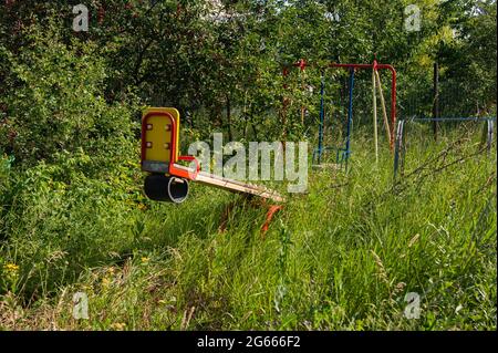 Eine überwuchert und verlassene Schaukel mitten im Wald. Viel Gras. Die Natur übernimmt. Seltsame Gefühle. Stockfoto