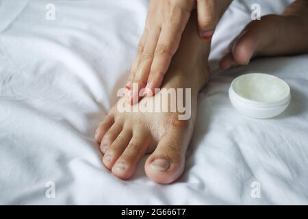 Frau, die Petroleum-Gelee auf die Füße auf dem Bett aufgibt Stockfoto