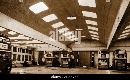 Ein altes britisches Pressefoto für Beton. Zeigt eine Busgarage mit einer dünnen gewölbten Gewölbedecke. Doppeldeckerbusse tragen Werbung für Scotch Whisky, Capstan Zigaretten etc. LINKS vom Bild IST EIN Mechaniker zu sehen, der an einer Bank arbeitet. Stockfoto