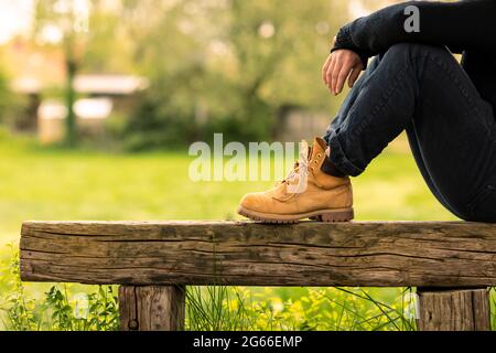 Ein Mann in legerer Kleidung sitzt auf einer alten Holzbank in einer ländlichen Gegend, während er über das Ackerland in der friedlichen idyllischen Landschaft blickt Stockfoto