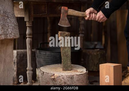 Holzfäller spaltete Holzstämme mit einer alten Axt auf einem großen Holzstumpf, um sie für seinen Kaminofen zu verwenden, während er sich selbst versorgte und das Holz lebte Stockfoto