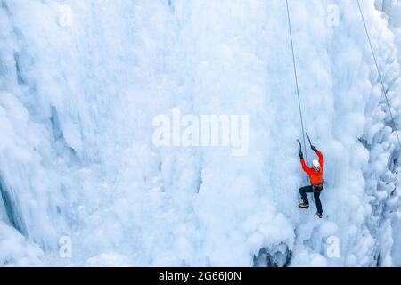 Luftaufnahme eines gefrorenen Wasserfalls und Felsen, bei dem Kletterer seine eisbedeckte Oberfläche mit Eispickeln und Steigeisen aufsteigen Stockfoto