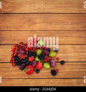Beerenmischung - Johannisbeeren, Stachelbeeren, Maulbeeren, Erdbeeren auf einem hölzernen Hintergrund mit Kopierfläche. Sommerkonzept. Stockfoto