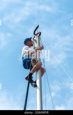 Mann in einem Sicherheitsgurt an der Spitze des Mastes einer Yacht oder eines Segelbootes, der Wartungsarbeiten an der Takelage durchführt, Großbritannien Stockfoto