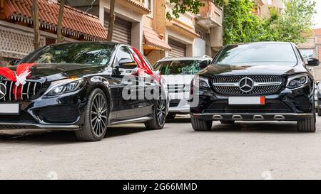 Low-Angle-Ansicht eines schwarzen Hochzeitswagens mit rotem Organza-Stoff und Schleife und schwarzem Mercedes 4matic. Stockfoto