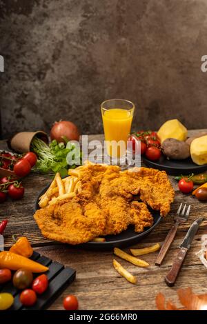 Goldfarbenes Schweinebraten mit gebratenen Pommes auf einem schwarzen Teller mit gemütl. Beilage auf dem Holztisch Stockfoto
