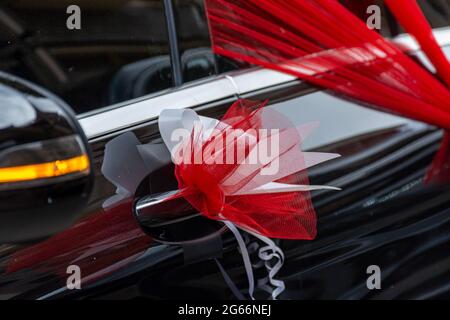 Schwarzes Hochzeitsauto, roter Organza-Stoff, Schleife. Stockfoto