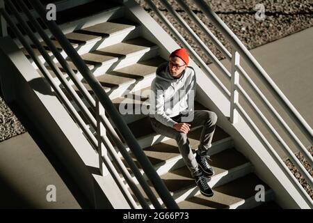 Männer Hipster allein auf Treppen in städtischen Gebäuden tragen trendige Brillen und Street-Fashion-Kleidung Stockfoto