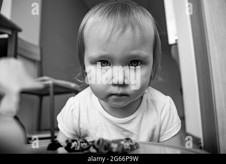 Ein schönes kleines kaukasisches Mädchen schaut ernsthaft mit großen Augen in den Rahmen. Porträt eines Kindes in schwarz-weiß. Stockfoto