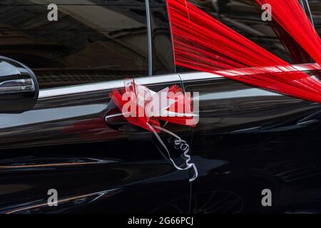 Schwarzes Hochzeitsauto, roter Organza-Stoff, Schleife. Stockfoto