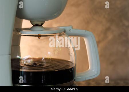 Kaffeekocher bei der Verarbeitung mit tropfendem Kaffee. Grauer Betonhintergrund mit warmem Licht. Kopierbereich. Stockfoto