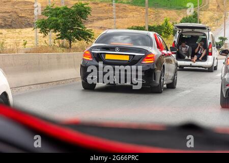 ar-Frontfenster-Ansicht eines schwarzen Hochzeitswagens auf der Autobahn mit rotem Organza-Stoff und Schleife. Stockfoto