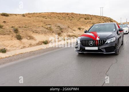 Low-Angle-Ansicht eines schwarzen Hochzeitswagens auf der Autobahn mit rotem Organza-Stoff und Schleife. Stockfoto