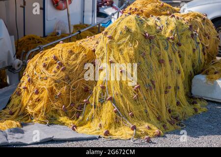 Die Fischernetze stapeln sich auf dem Fischerhafen und trocknen unter der Sonne. Gelbe Fischnetze mit Seilen und Schwimmern. Griechische Insel Kykladen Fischer Ausrüstung Stockfoto