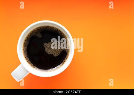 Draufsicht auf schwarzen Kaffeebecher mit Blasen auf der Oberseite, auf hellorangefarbenem Hintergrund platziert. Eine Tasse Kaffee hebt sich ab. Speicherplatz kopieren. Stockfoto