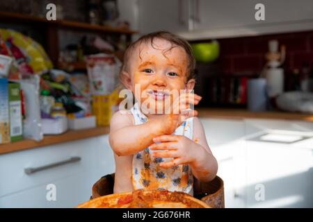 Ein Baby, das auf einem Hochstuhl sitzt, nachdem es unordentlich gegessen hat Stockfoto