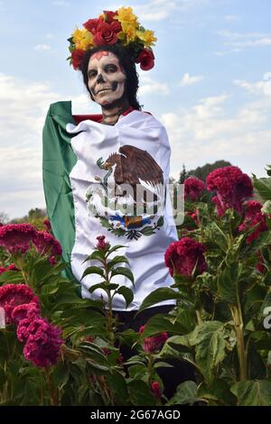 Eine Frau, die als Catrina gekleidet ist, eine berühmte Day of the Dead Figur, posiert in einem Feld von Day of the Dead Blumen. Stockfoto