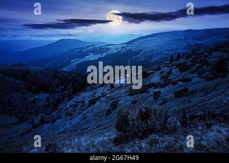 karpaten-Berglandschaft bei Nacht. Wunderschöne Landschaft mit grünen Hügeln im Vollmondlicht unter Wolken am dunklen Himmel im Sommer. Beliebt Stockfoto