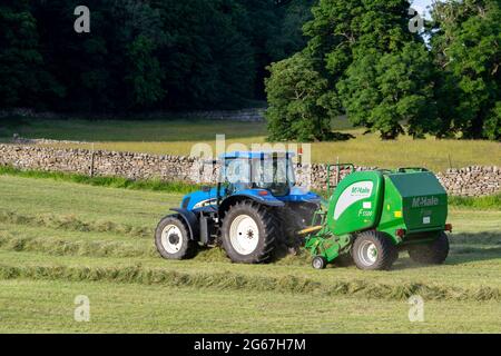 Landwirt, der große runde Heuballen mit einem New Holland TS135 Traktor und einer McHale F5500 Ballenpresse macht, am Sommerabend in Wensleydale, North Yorkshire Stockfoto