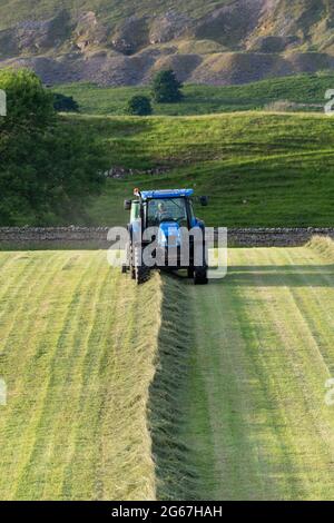 Landwirt, der große runde Heuballen mit einem New Holland TS135 Traktor und einer McHale F5500 Ballenpresse macht, am Sommerabend in Wensleydale, North Yorkshire Stockfoto