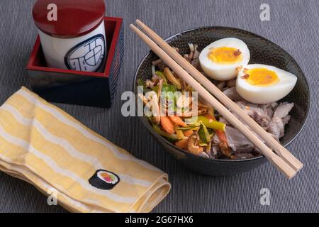 Studio Schuss von schwarzen Schüssel Ramen Nudeln mit gekochten Eiern, Gemüse und truthahn treffen, bereit, mit kochender Brühe gegossen werden. Essstäbchen aus Holz Stockfoto