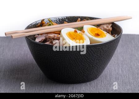 Studio Schuss von schwarzen Schüssel Ramen Nudeln mit gekochten Eiern, Gemüse und truthahn treffen, bereit, mit kochender Brühe gegossen werden. Essstäbchen aus Holz Stockfoto