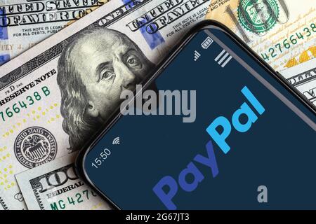 Moskau - 10. Juni 2021: PayPal-Logo auf dem Smartphone-Bildschirm und Dollarnoten, digitale App für die Zahlung im Handy. Konzept des virtuellen Geldes, paypal s Stockfoto
