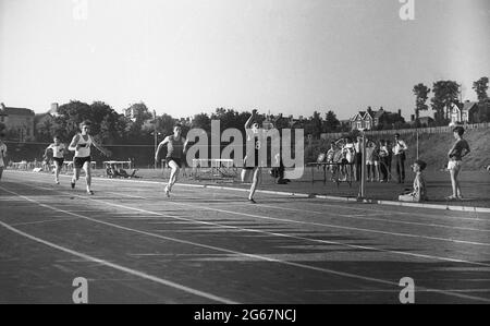 1960s, historischer Tag, Leichtathletik, Sporttag zwischen den Bezirken, junge Männer, die auf einer Schlagerbahn in einem Sprint-Rennen draußen antreten, England, Großbritannien. Stockfoto